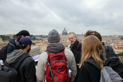 Professor lecturing students with Vatican dome in the background.