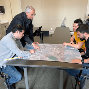 Senior Research Associate Carl Elefante speaking with three MSHP students in a classroom, pointing at a large printed diagram.