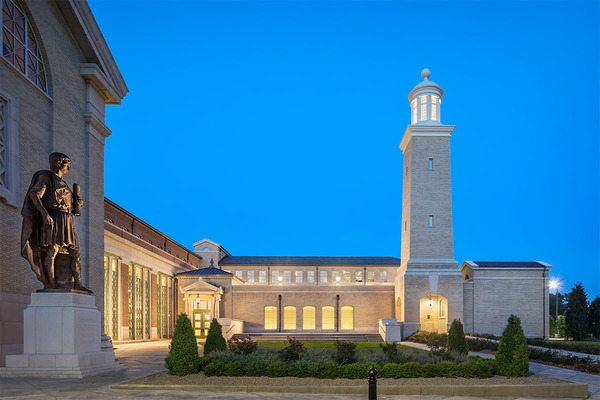 Image of Matthew and Joyce Walsh Family Hall of Architecture outside with tower to the right, the lights on from inside create a glow against a blue background.