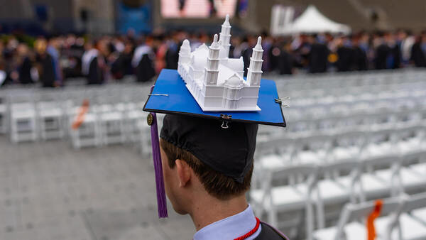 A graduate's black cap is adorned with a white 3D model during commencement.